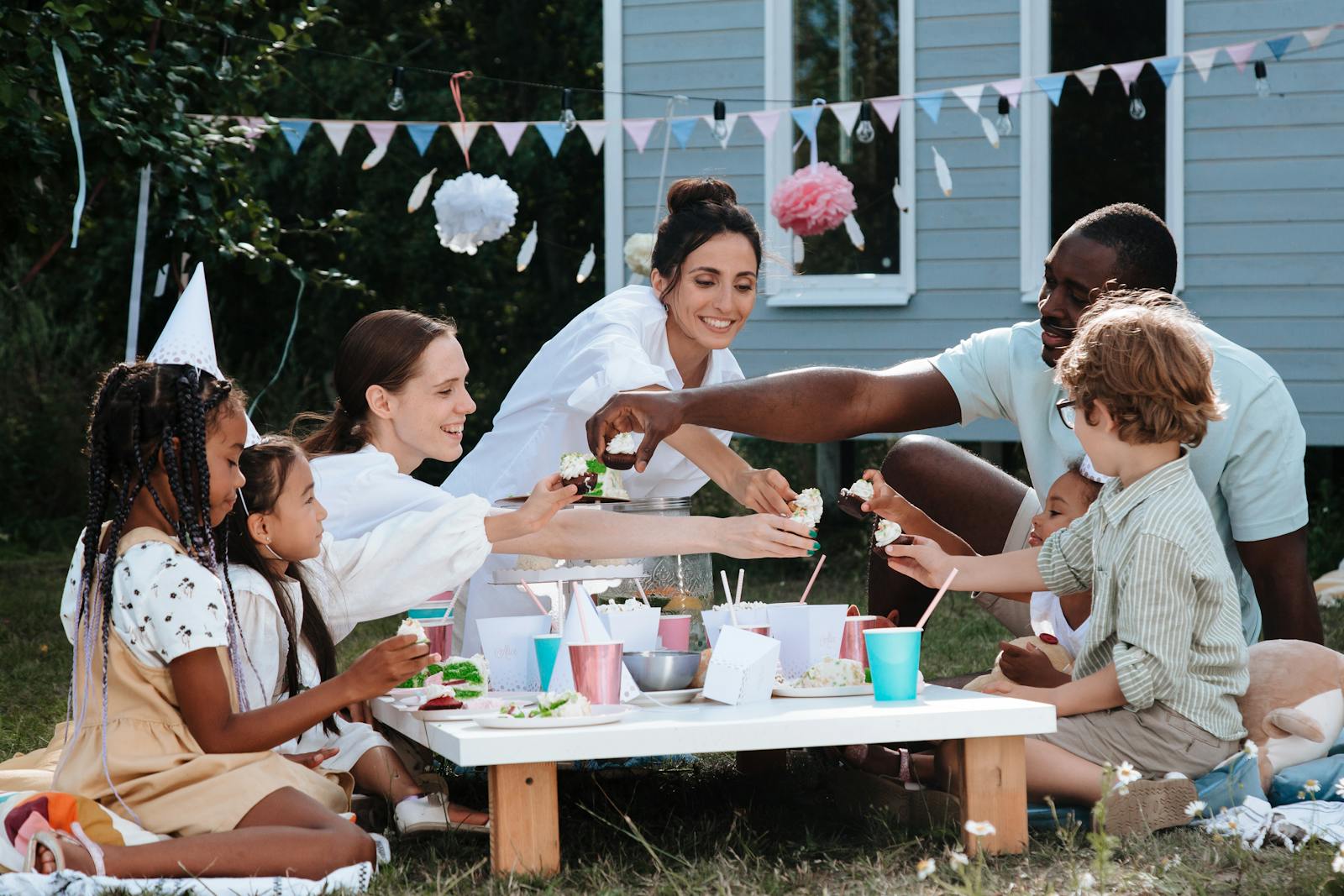 A lively backyard picnic with diverse family and friends sharing food outdoors on a sunny day.
