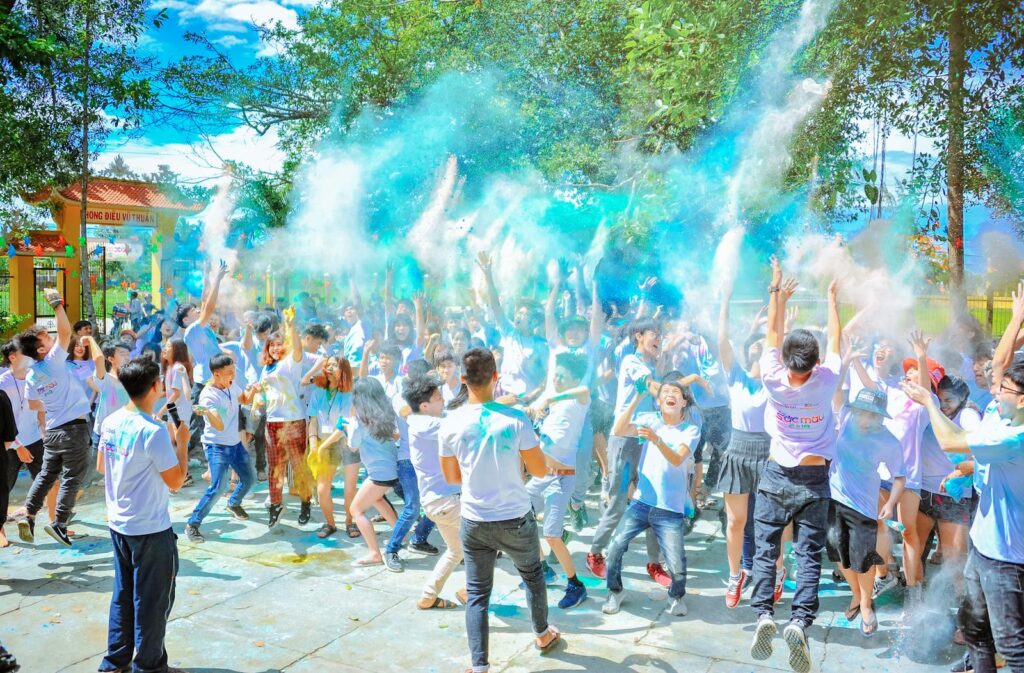 Energetic crowd enjoying a vibrant outdoor festival with colorful powder at daytime.